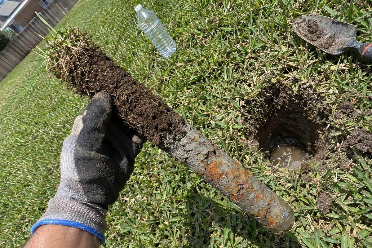 A gloved hand holding a soil core, brown topsoil at one end turning to gray clay with rust mottles